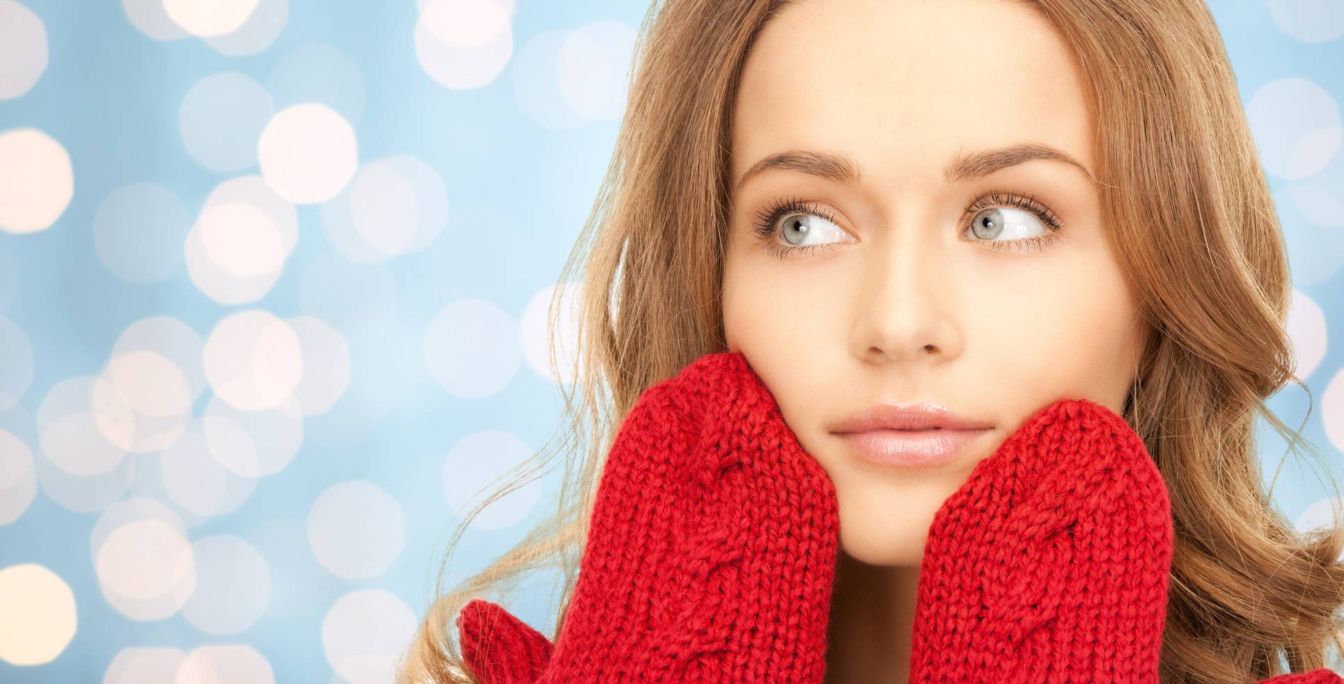 happiness, winter holidays, christmas and people concept - happy young woman in red mittens touching her face over blue lights background